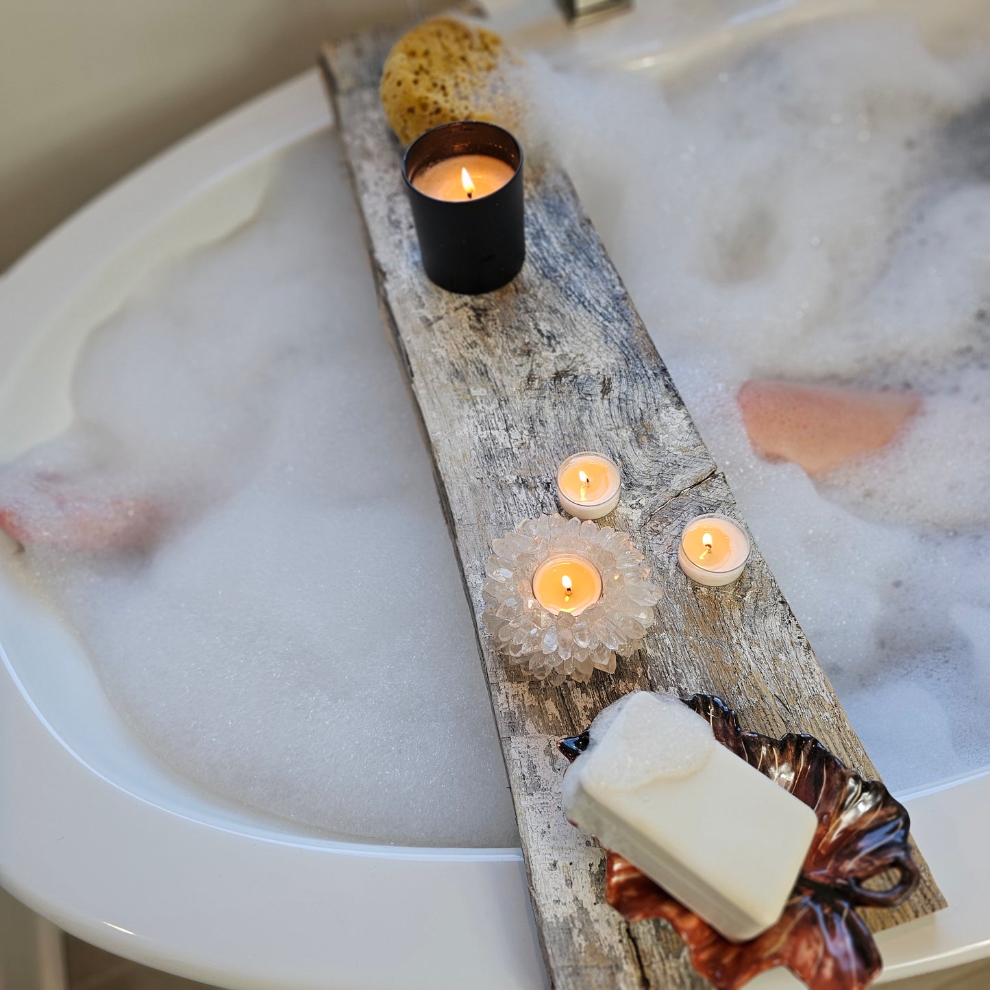 Bath setup with candles, soap, and a decorative log in a bathtub filled with bubbles.
