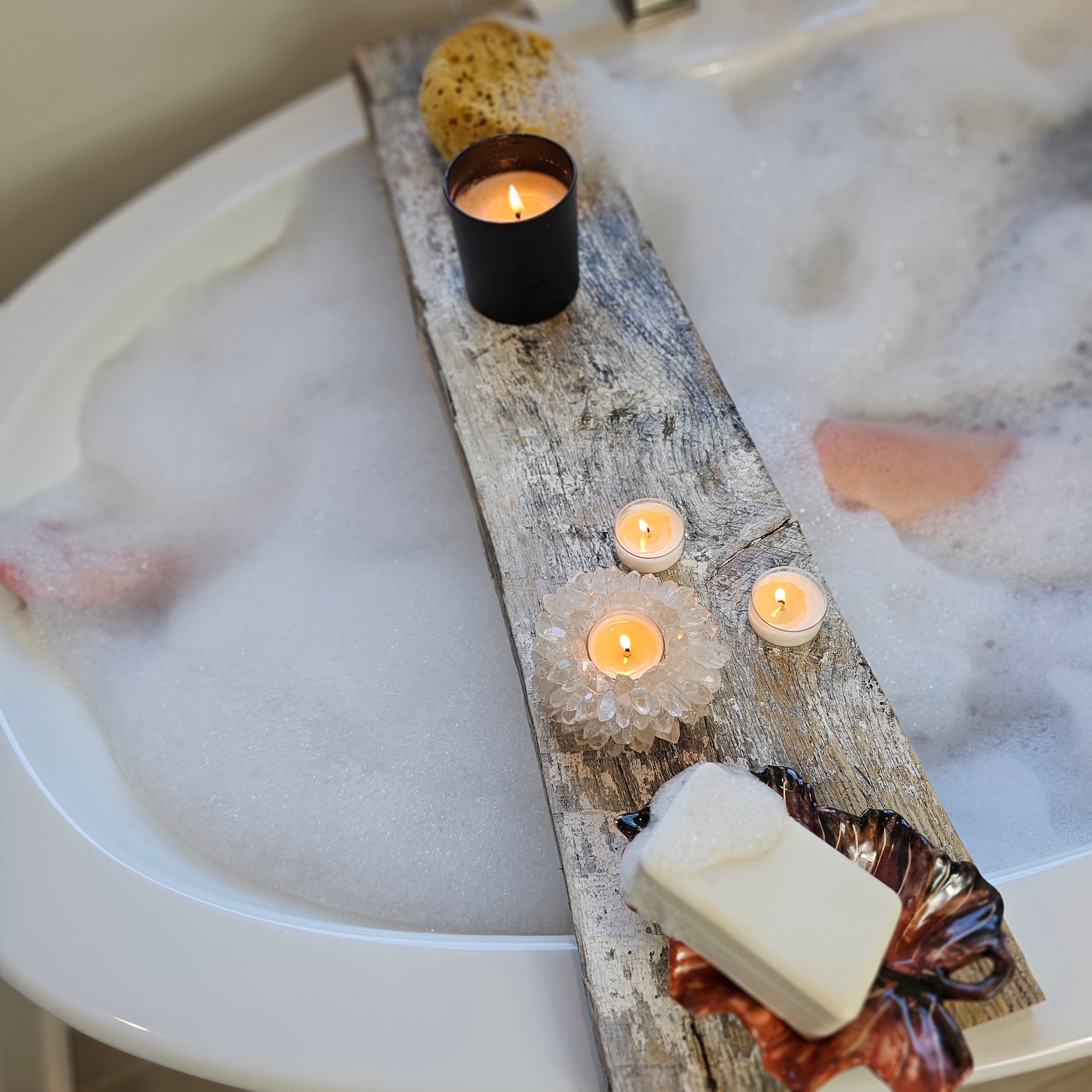 Bath setup with candles, soap, and a decorative log in a bathtub filled with bubbles.