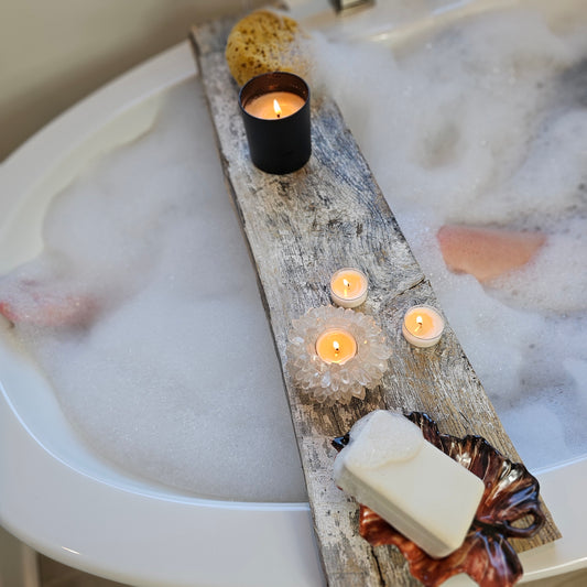 Bath setup with candles, soap, and a decorative log in a bathtub filled with bubbles.