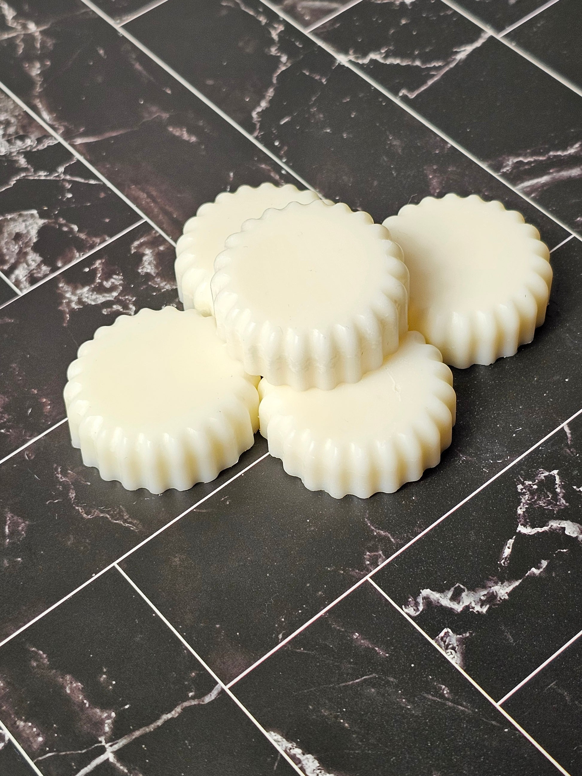 Five wax melts on a dark marble background